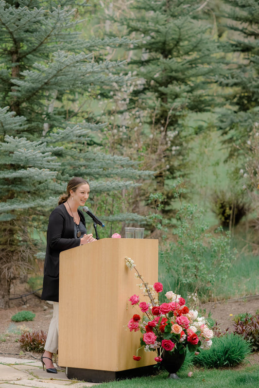 Magi Fisher speaking at a podium in the forest for WIPA ceremony.